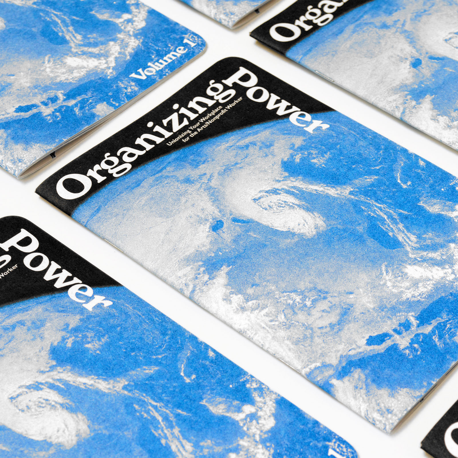 Multiple copies of the Organizing Power, Volume 1 booklet with a blue-and-white satellite image of Earth on the cover, arranged on a white surface.