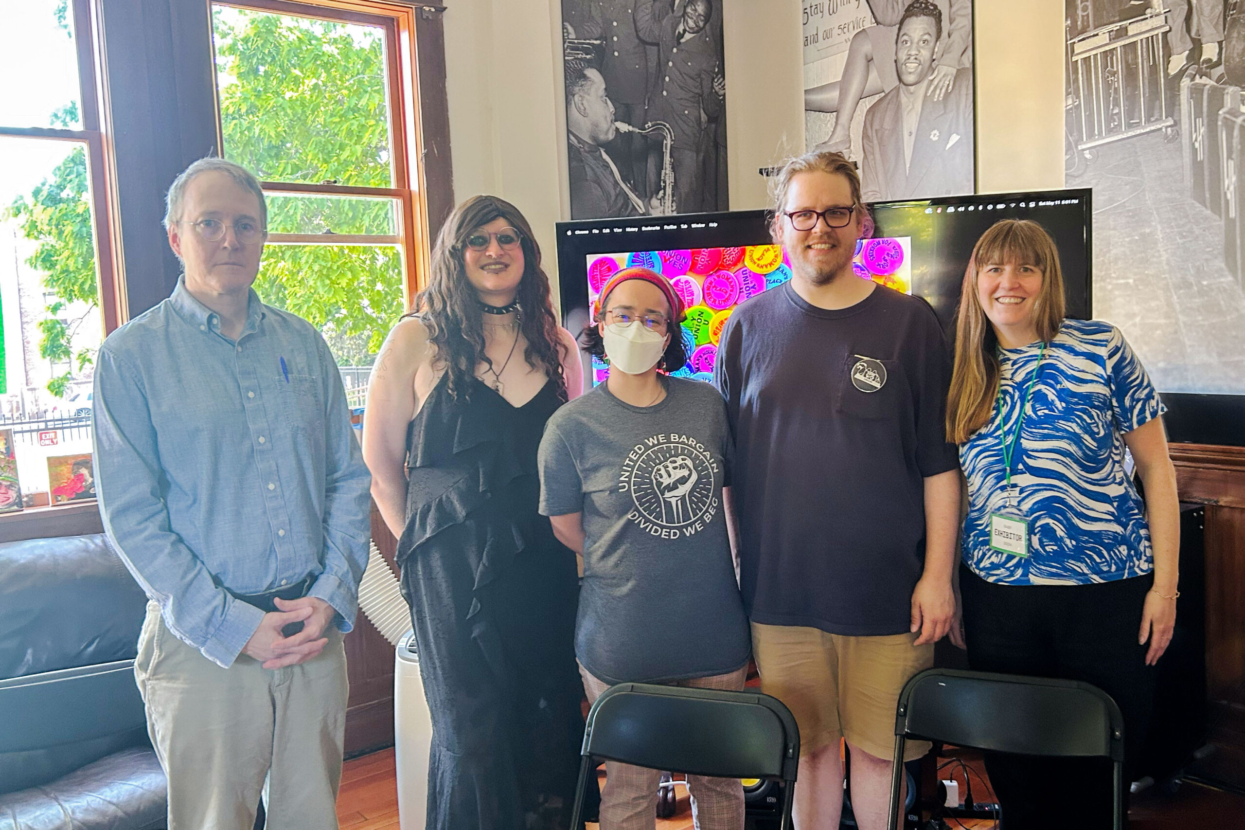 Five panelists standing together after the Organizing Power roundtable at the Seattle Art Book Fair, May 2024. One participant wears a 'United We Bargain, Divided We Beg' t-shirt. A screen displaying colorful pro-union buttons is visible behind the group.